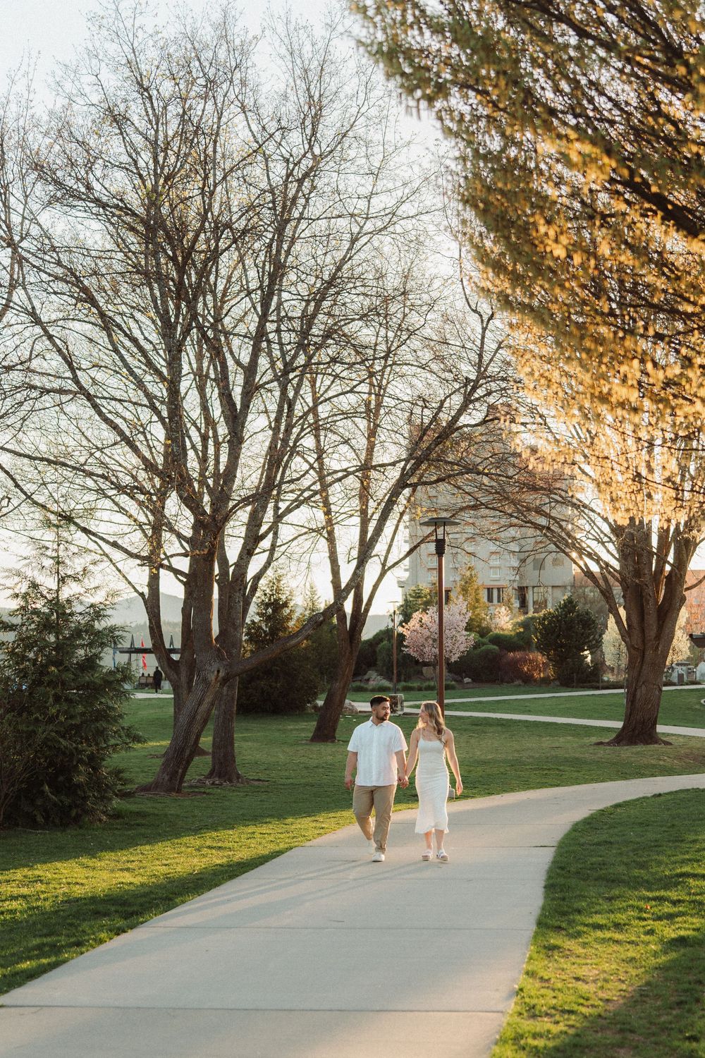 Couple holding hands while walking on a park path at sunset.
