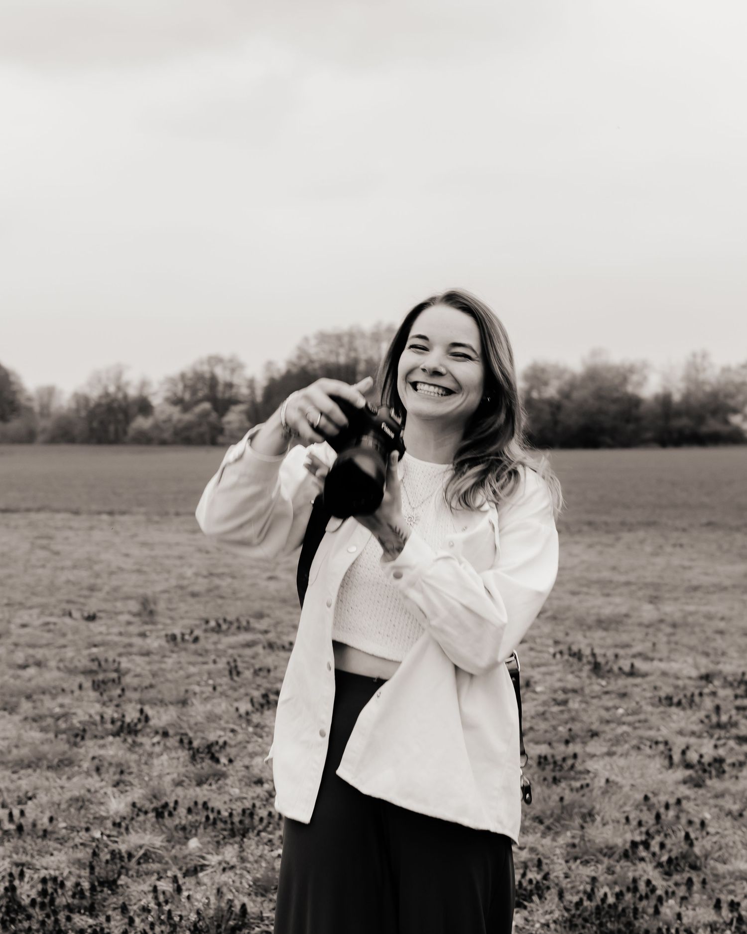 Smiling young woman holding a small black dog in an open field, wearing a white shirt and black skirt.