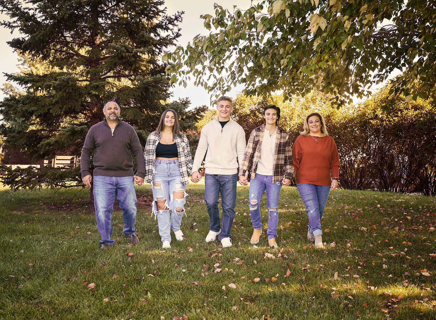 Family of five with three teenagers hand-in-hand strolling down a hill