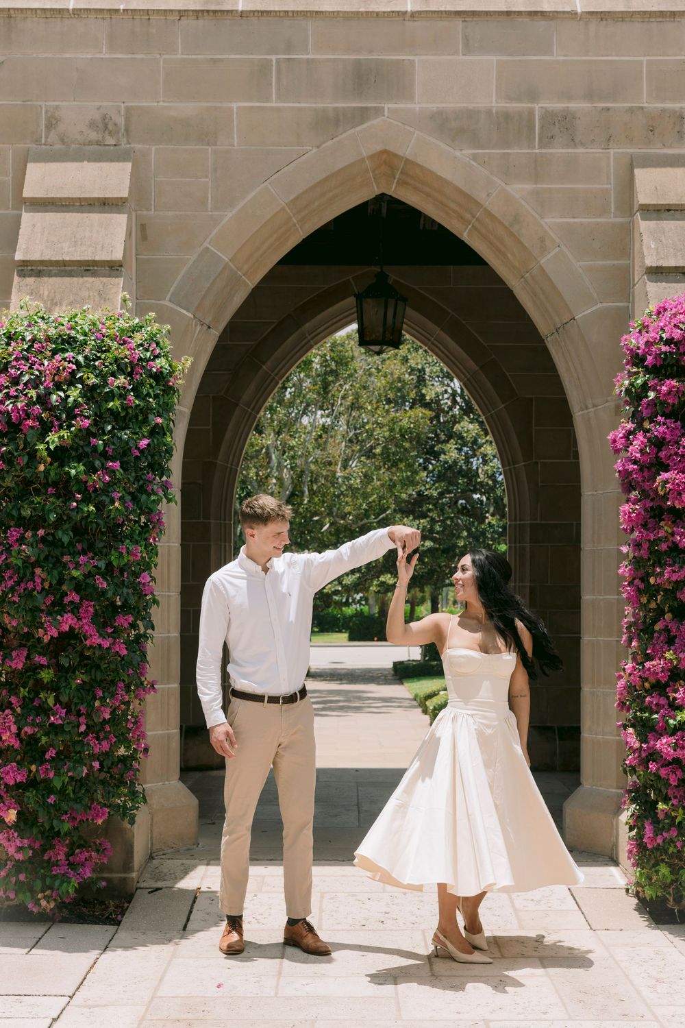 Couple dancing under a Gothic stone arch surrounded by vibrant pink bougainvillea flowers on a sunny day.