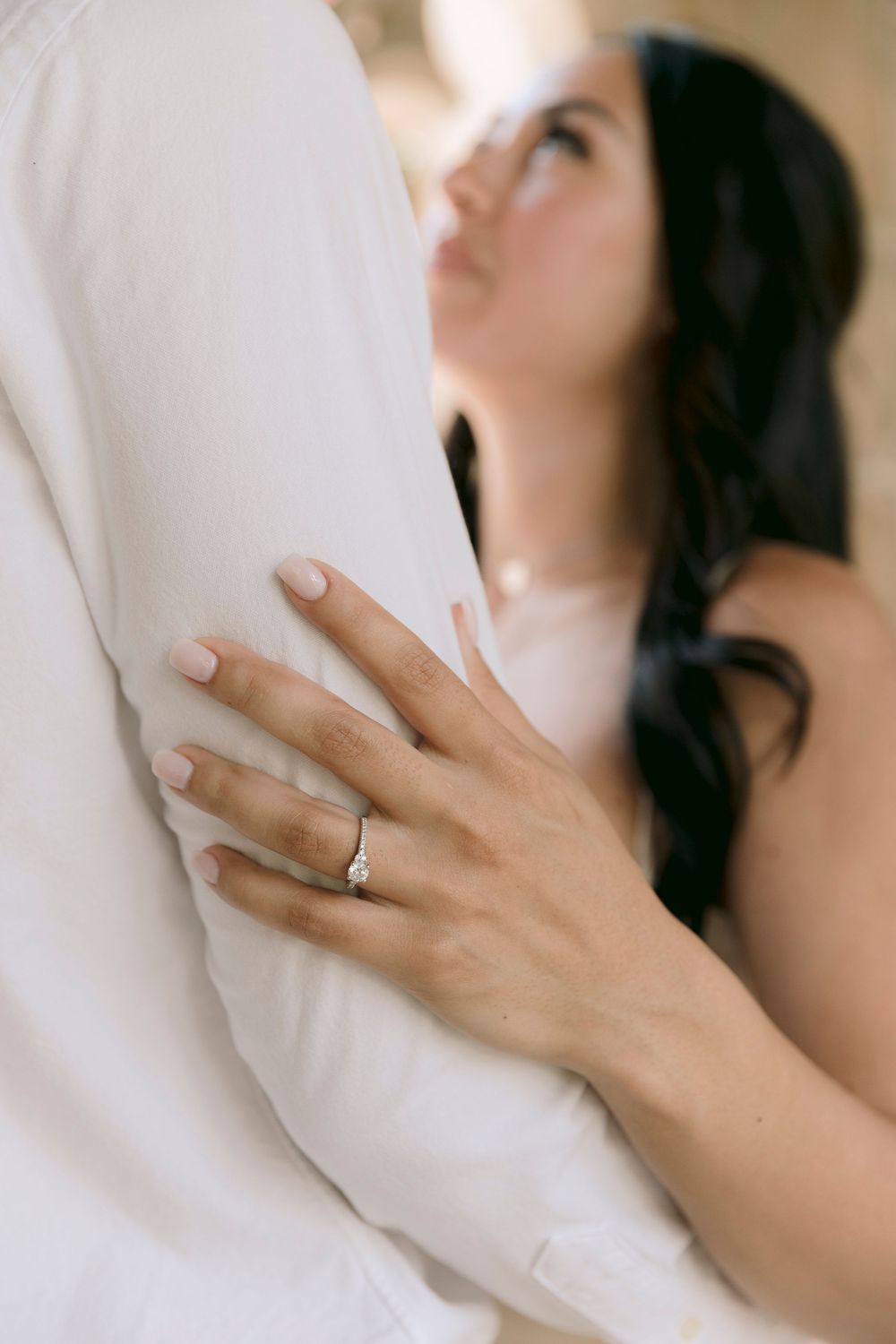 Close-up of a woman's hand with a diamond engagement ring resting on a man's white shirt.