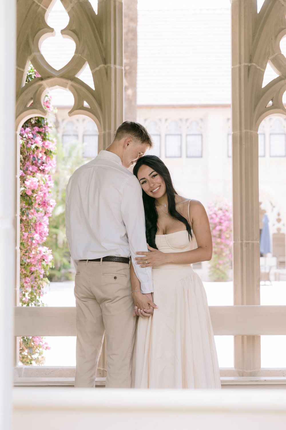 Couple in elegant attire sharing a tender moment under Gothic arches with pink bougainvillea blooms.