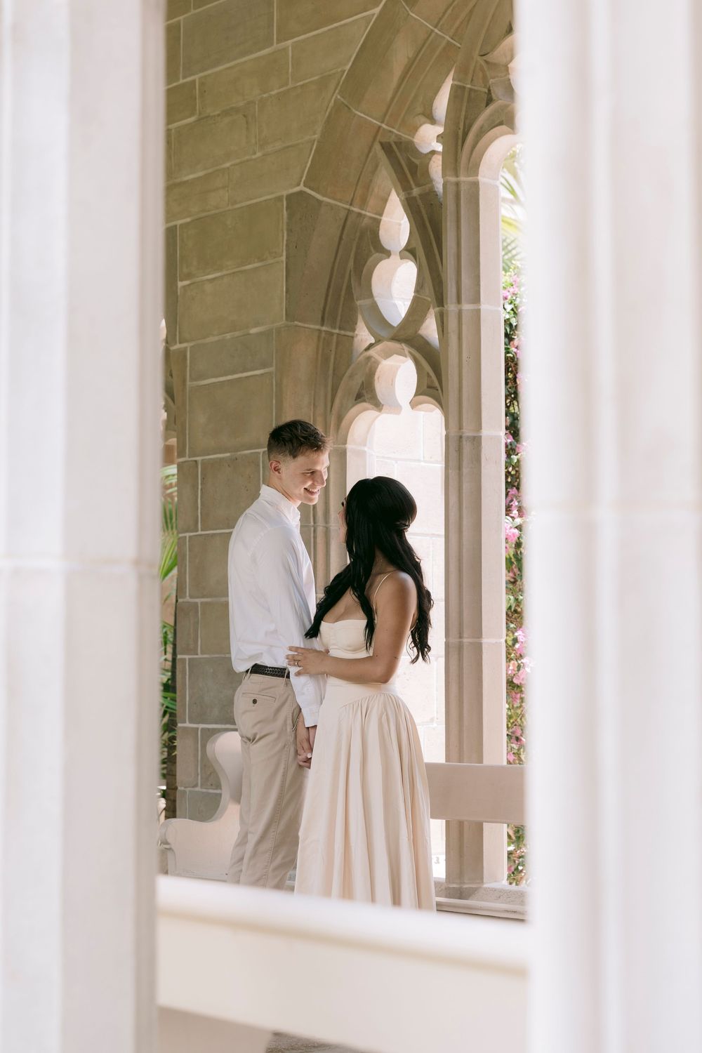 Couple sharing a romantic moment under Gothic stone arches surrounded by lush greenery.