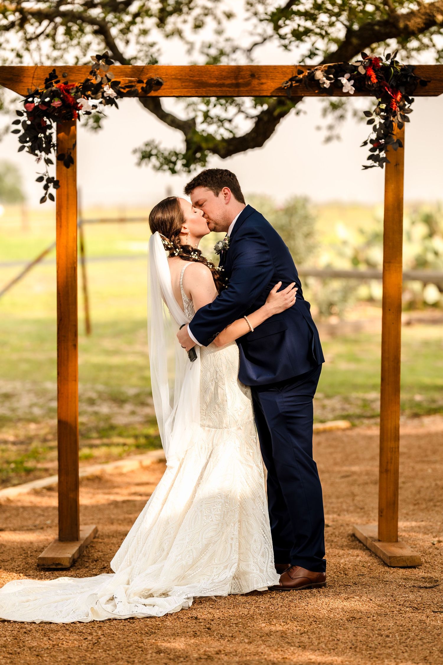 Intimate wedding portrait of a bride and groom kissing under a rustic wooden arch during an outdoor ceremony in Central Texas.