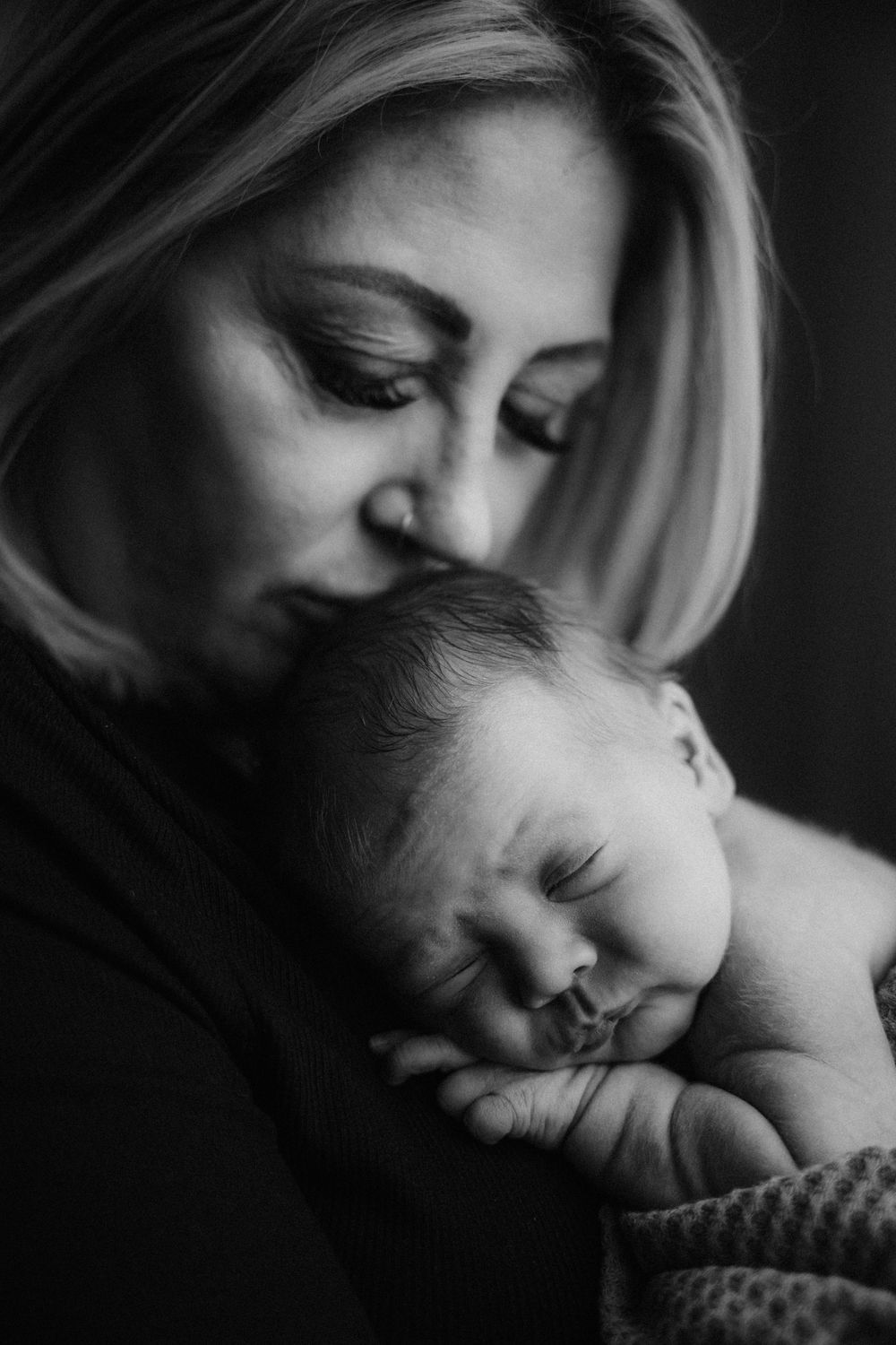 Black and white portrait of a mother tenderly holding her sleeping newborn baby close to her face.