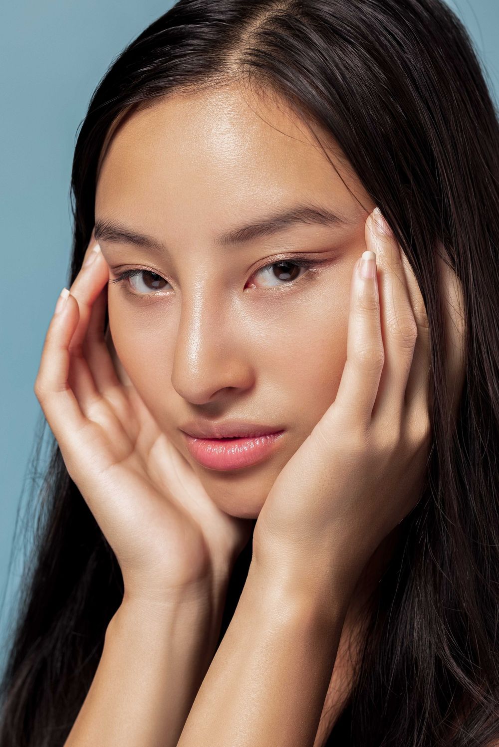Beauty closeup showing dewy skin and natural makeup against blue background.