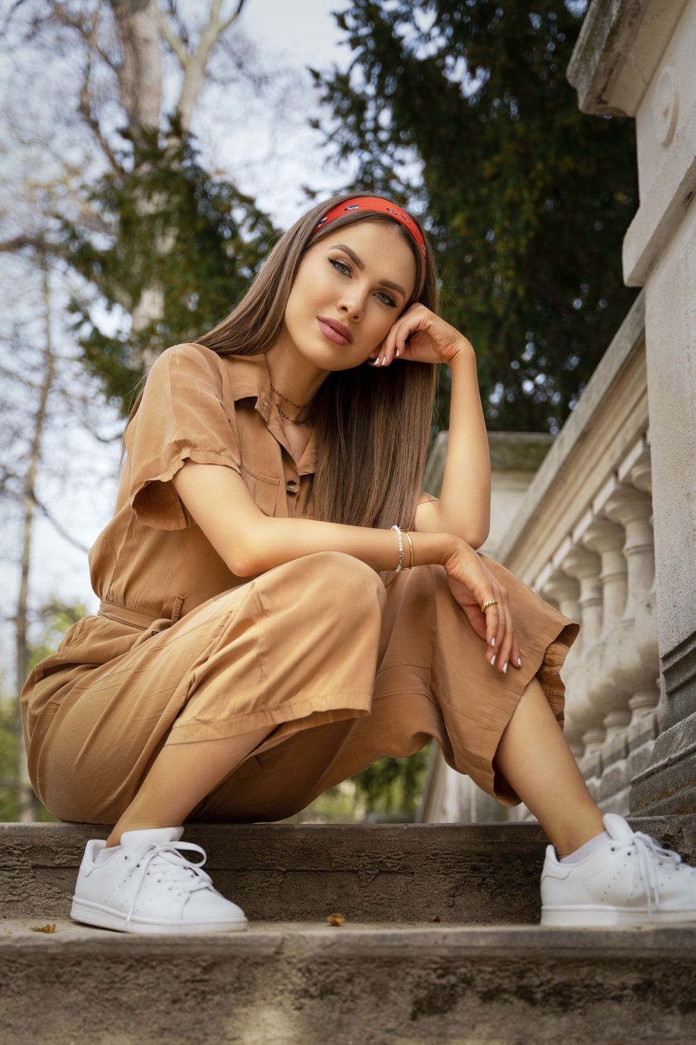 Casual fashion poses in a tan dress and white sneakers on stone steps.