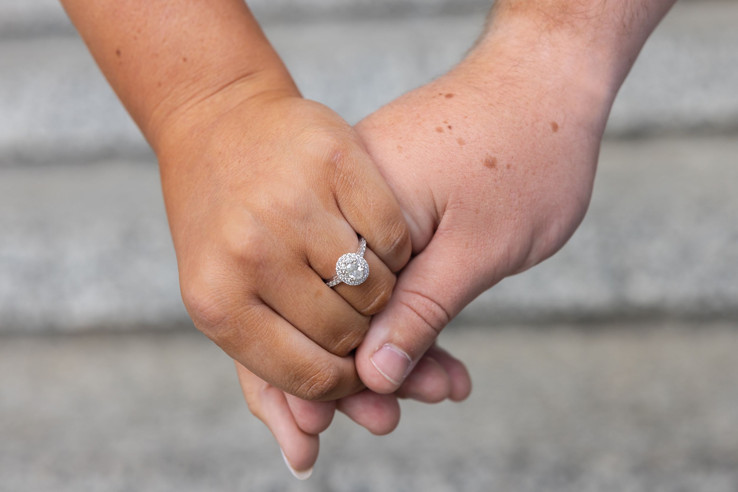Close-up of two hands intertwined, one wearing a sparkling diamond halo engagement ring.
