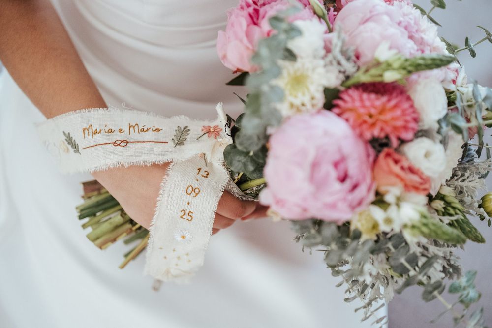 Bride holding a colorful wedding bouquet with pink peonies and a ribbon reading Maria and Mario with their wedding date.