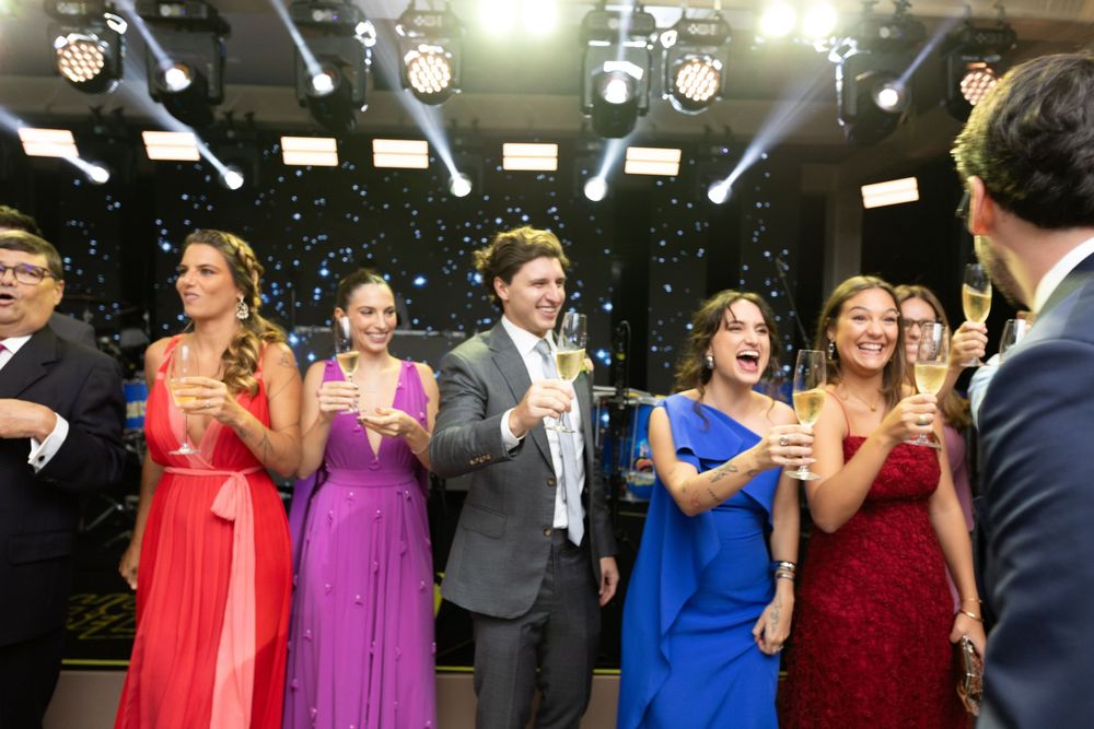 Elegantly dressed guests in colorful gowns toast with champagne glasses at a glamorous formal celebration event.