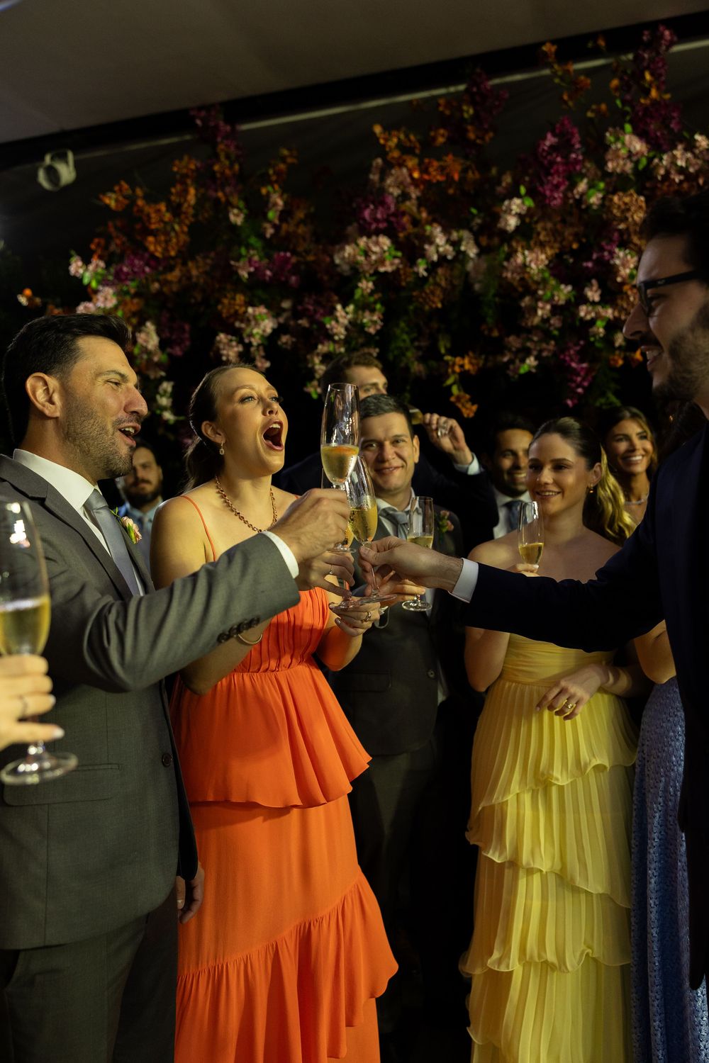 Guests in formal attire toasting with champagne glasses at an elegant celebration with floral decor.
