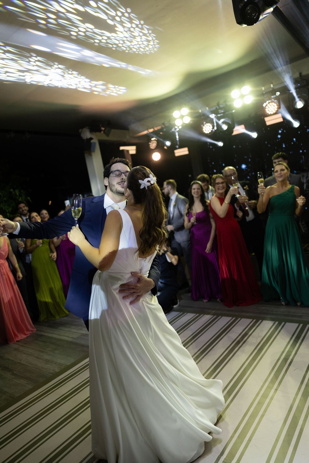 Bride and groom share first dance at elegant wedding reception with colorful bridesmaids watching in background.