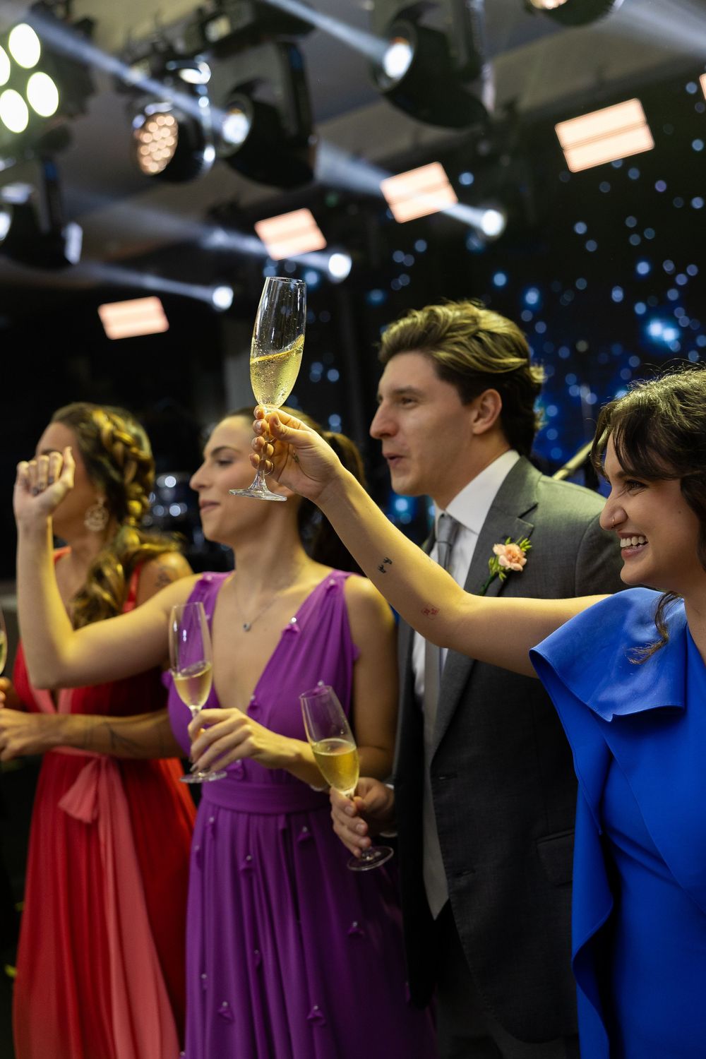 Elegantly dressed guests raising champagne glasses in a toast at a formal event under stage lights.