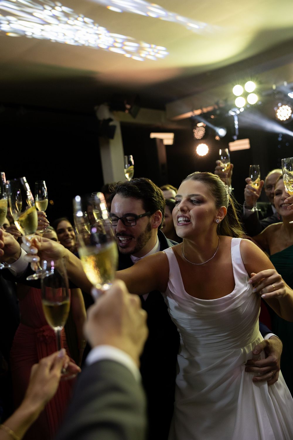 Bride and groom celebrate with champagne toast surrounded by cheering wedding guests at reception.