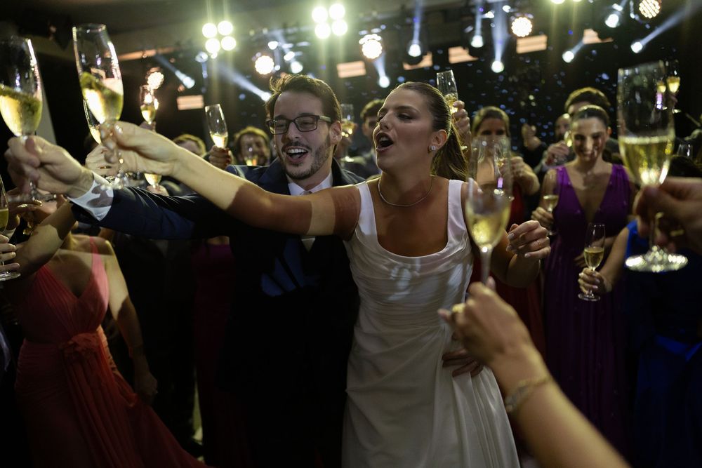 Joyful bride and groom toasting with champagne glasses surrounded by guests at a lively wedding reception.
