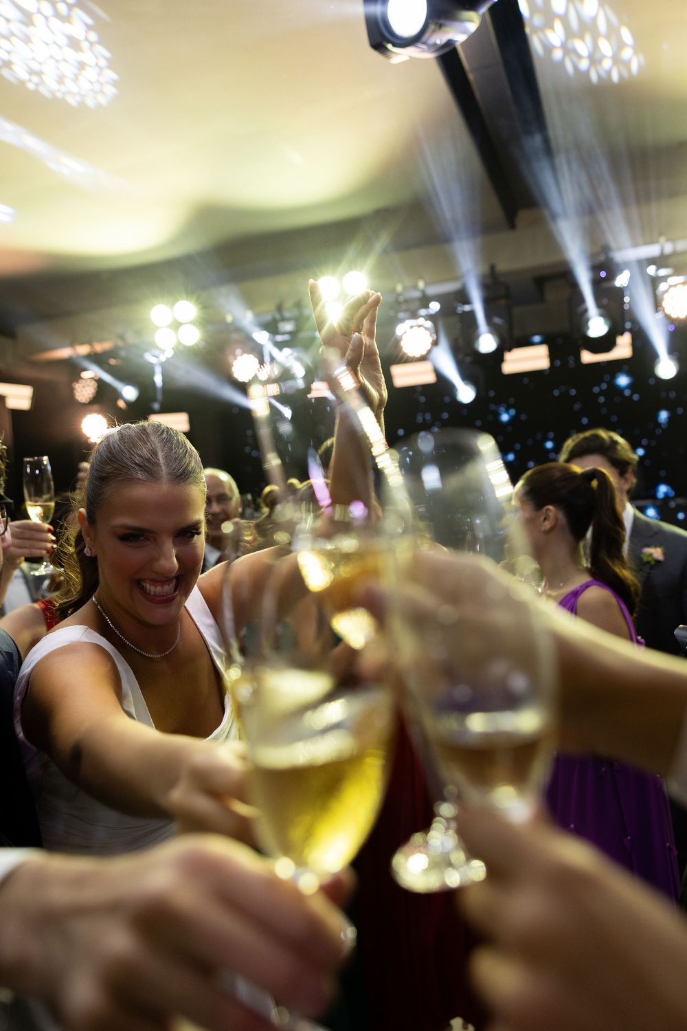 Excited guests toasting with champagne glasses at a glamorous party with stage lighting.