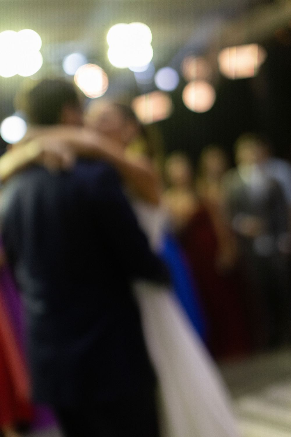Blurry romantic first dance of bride and groom at wedding reception with soft bokeh lights and guests in background.
