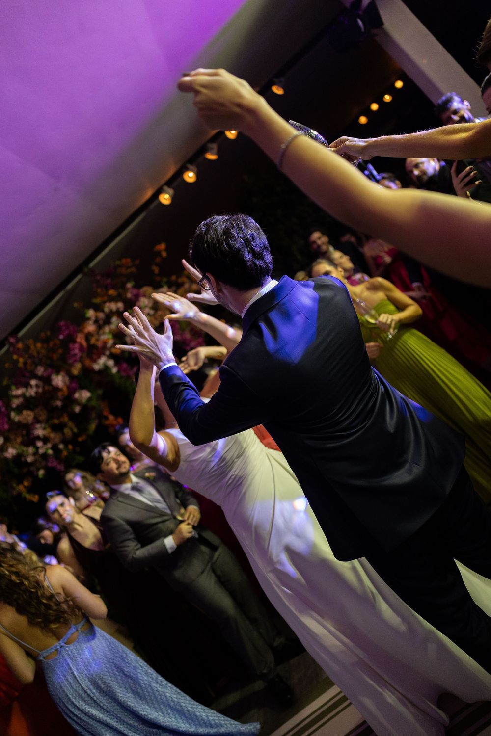 Couple dancing at elegant wedding reception with guests watching under purple lights.