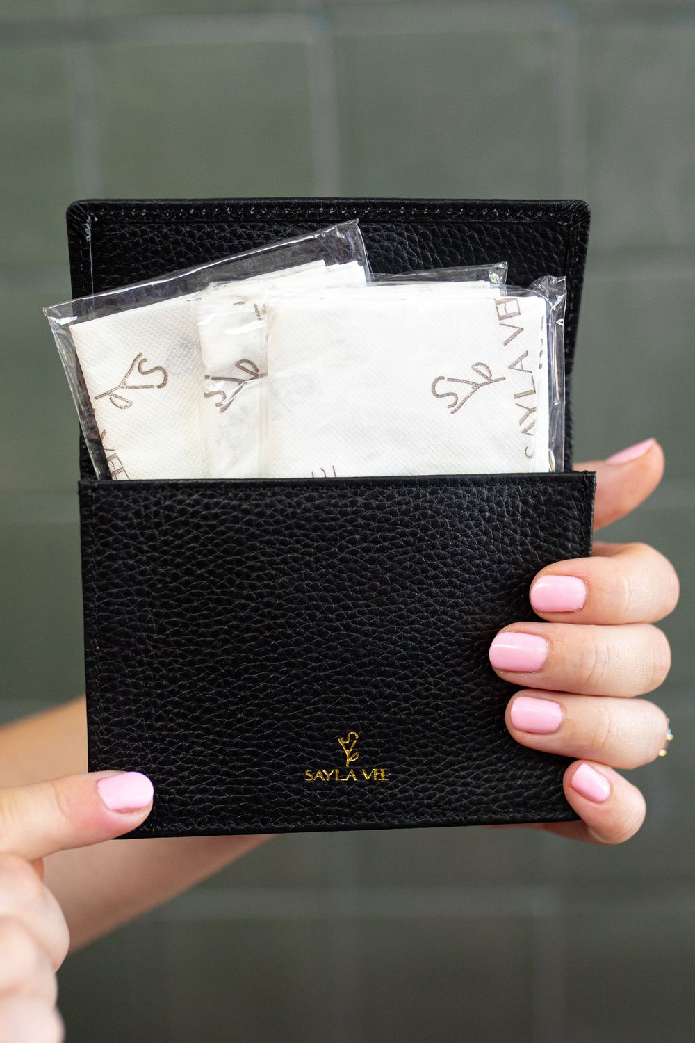 Sayla Vie black pebbled leather wallet held open displaying branded tissue paper packets inside.