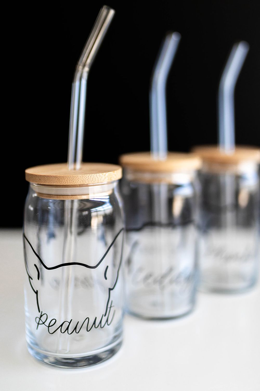 Personalized glass can cups with bamboo lids and metal straws, featuring dog outline designs and names like Peanut.