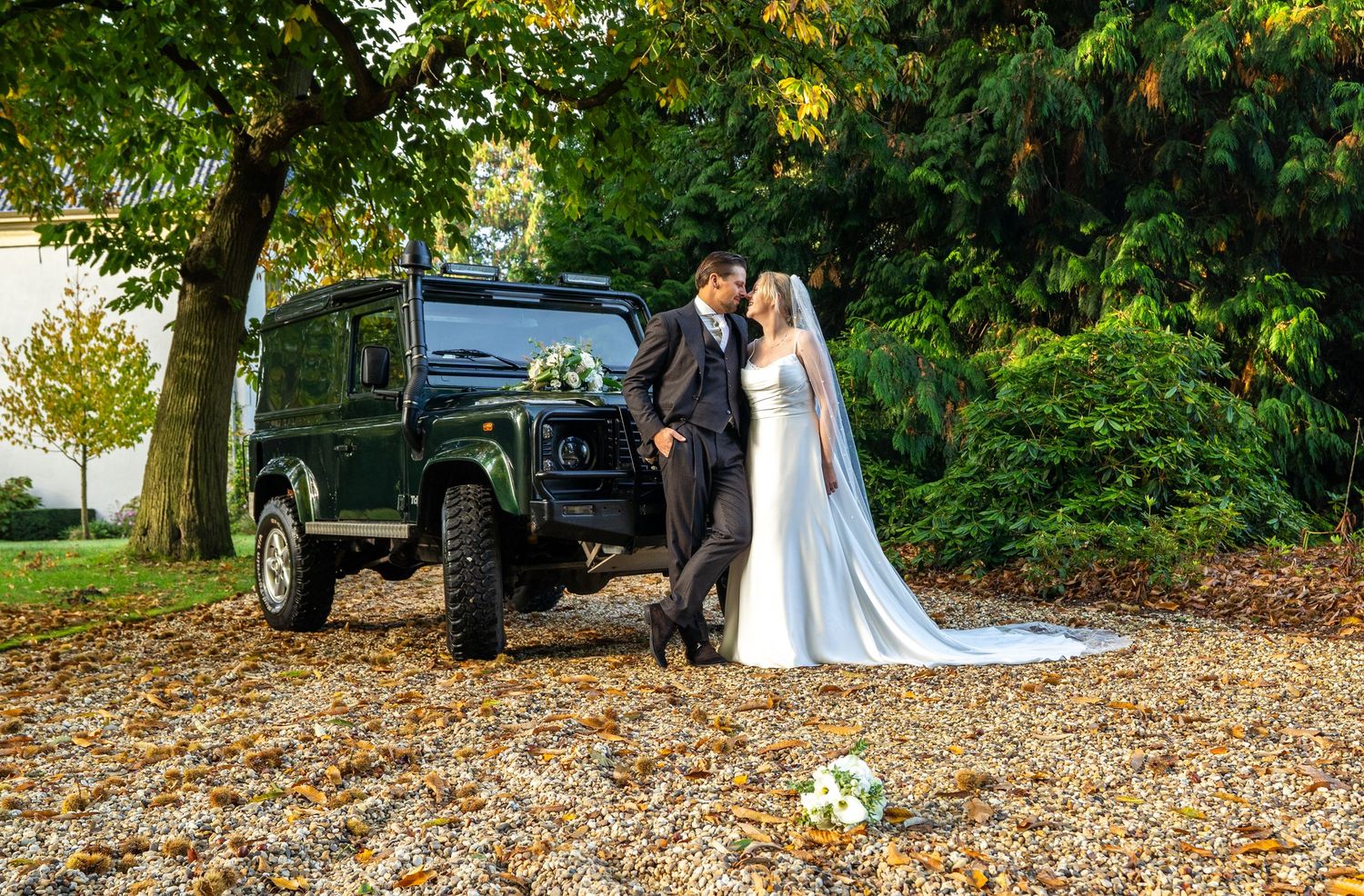 Bruid en bruidegom delen een romantische kus naast een vintage Land Rover Defender op een herfstachtige dag door bruidsfotograaf Heerde