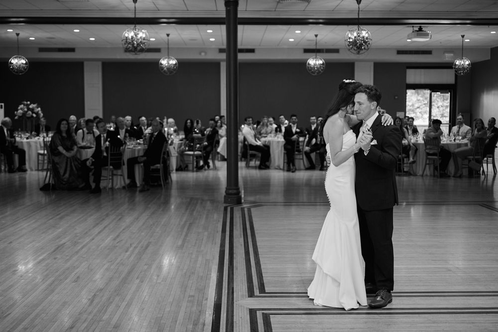 Bride and groom share their first dance on a wooden dance floor at an elegant wedding reception in black and white.