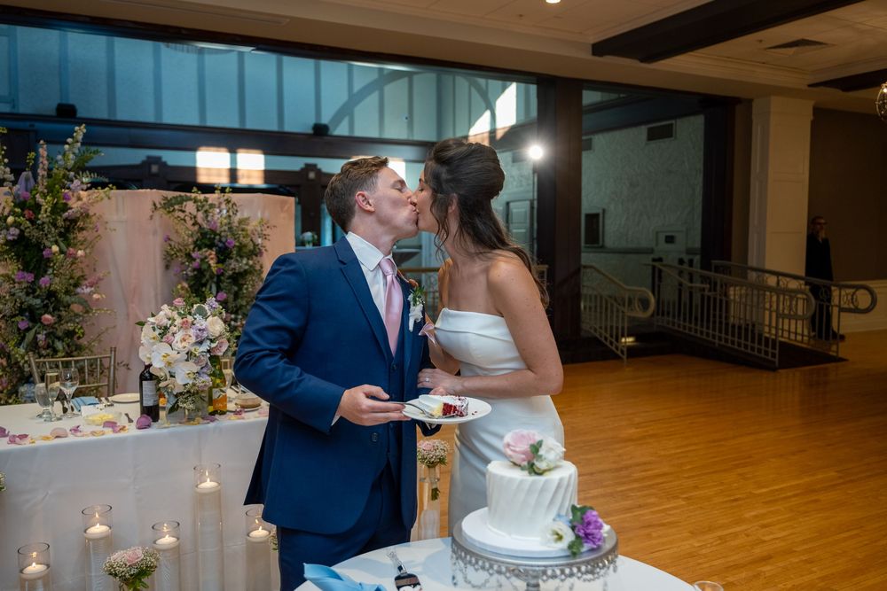 Bride and groom share a kiss while cutting their white wedding cake at a romantic indoor reception venue.