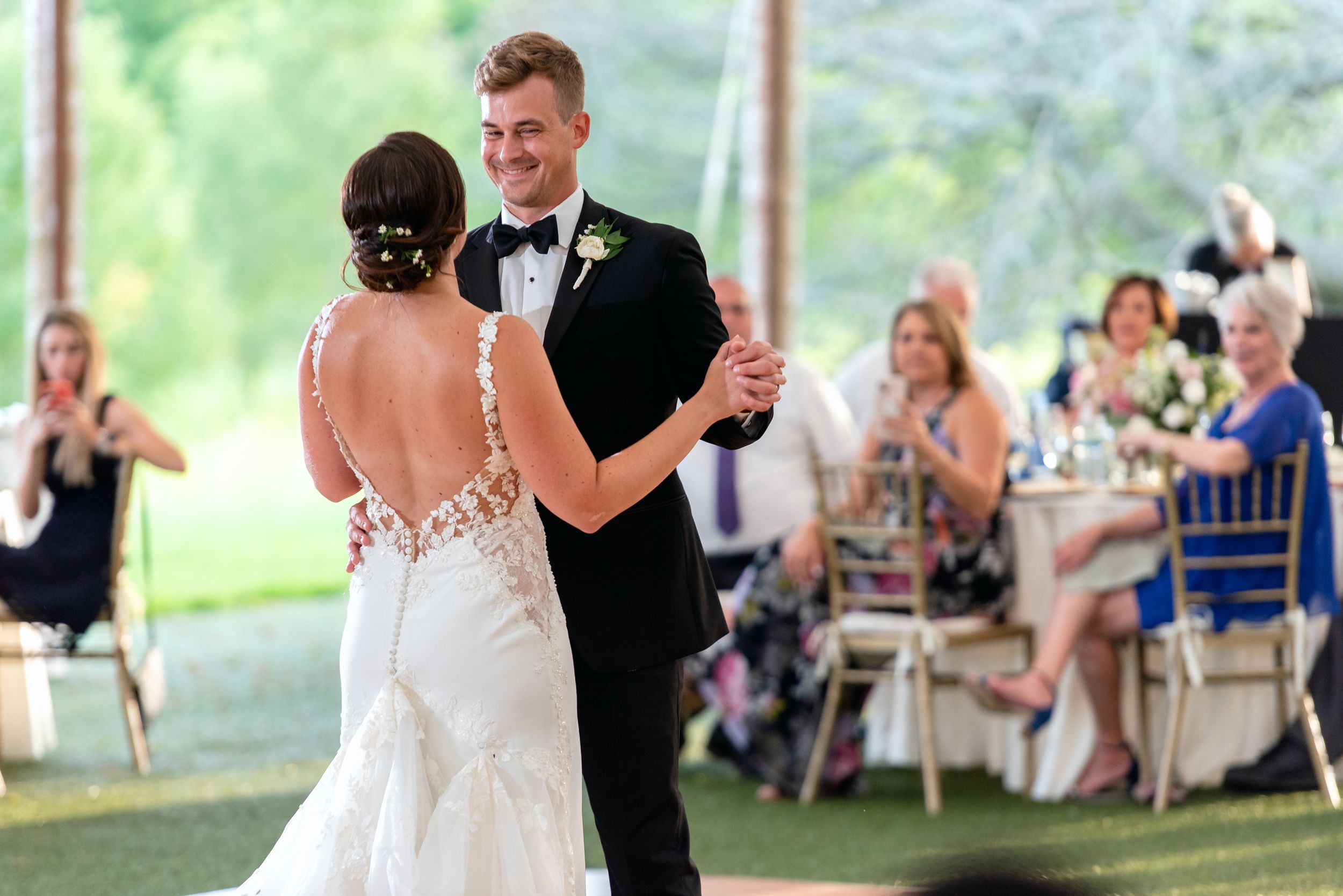 Bride and groom share their first dance at an elegant outdoor wedding reception with guests seated at tables.