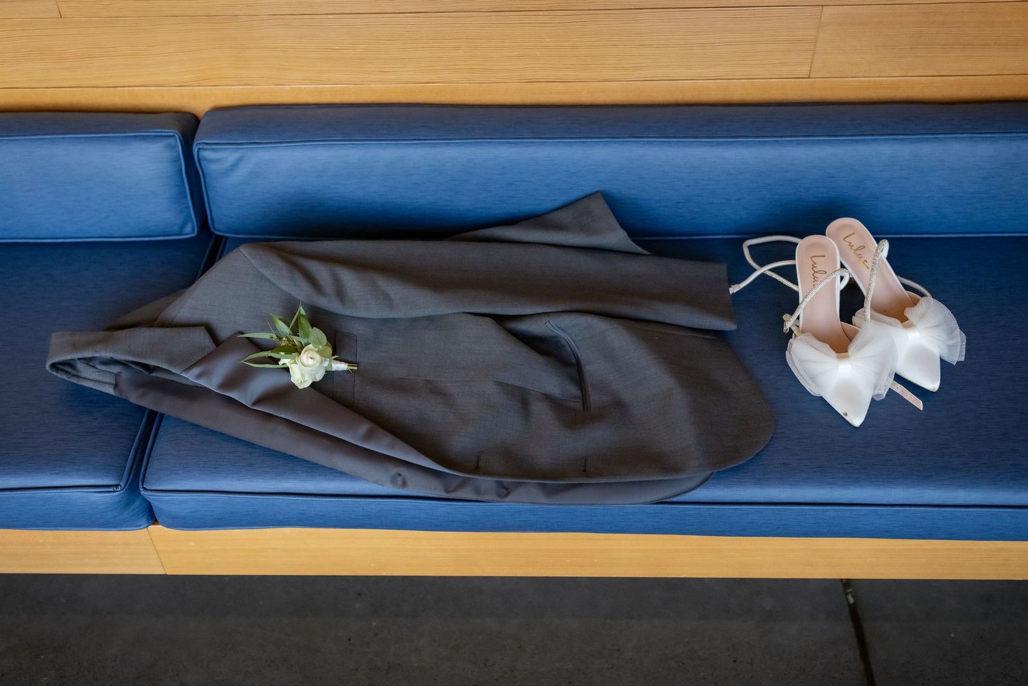 Dark suit with boutonniere and white heels on a blue bench at a wedding venue.