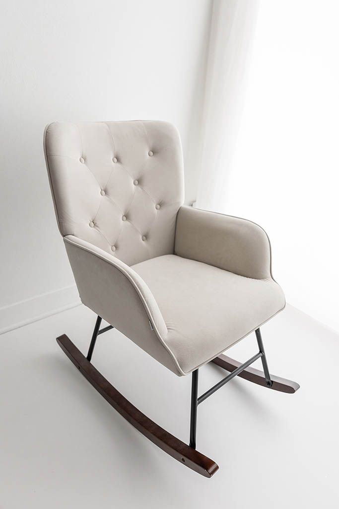 Newborn studio seating in Menifee; Beige tufted velvet rocking chair with dark wood curved rockers near window.