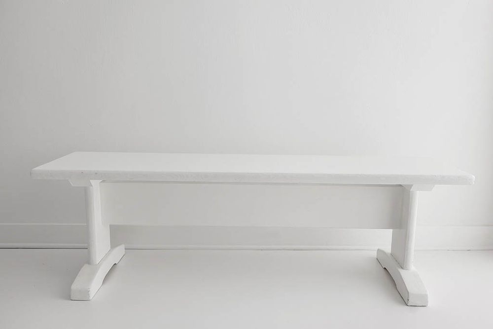 White painted wooden trestle bench against a white wall background.
