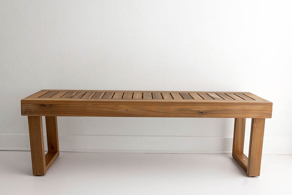 Natural teak wooden slat bench with block legs against a white wall.