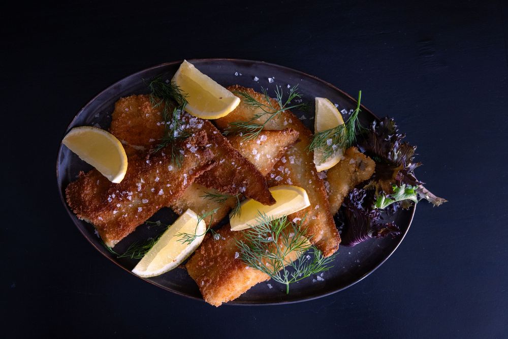 Crispy salmon fillets garnished with fresh dill and lemon wedges served on a dark oval plate.