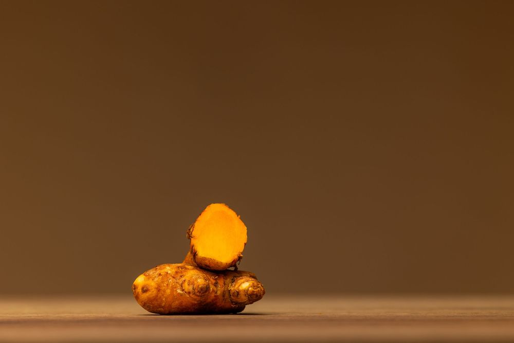 Fresh turmeric root with a cross-section slice revealing vibrant orange flesh on a wooden surface.