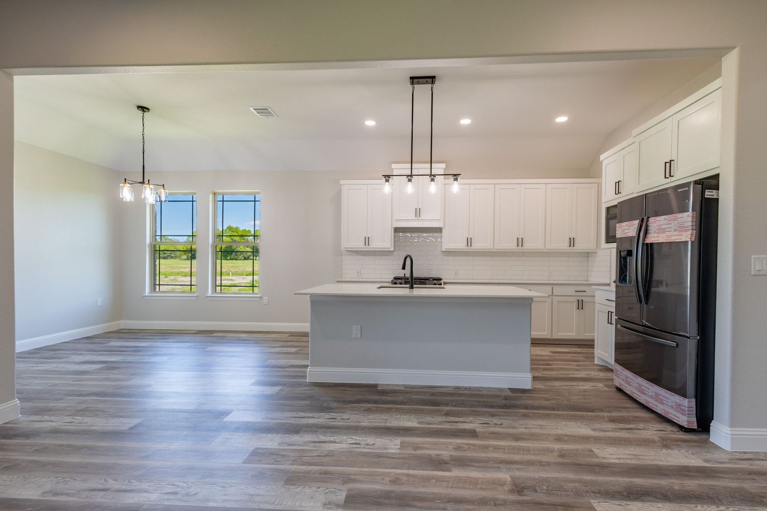 Modern open concept kitchen with gray floors, white cabinets and large windows.