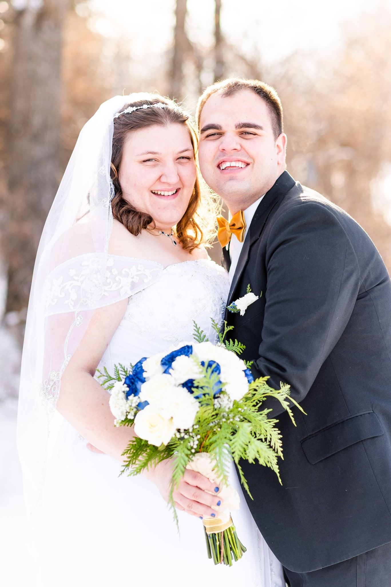 Bride and groom sharing a kiss in a snowy winter setting, bride holding blue and white bouquet wearing lace gown and veil.