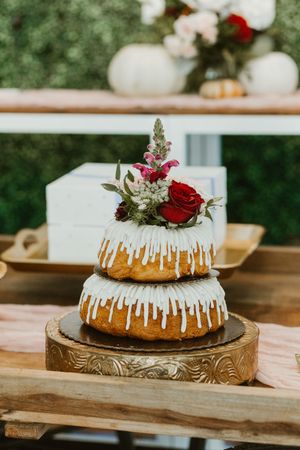Two-tier bundt wedding cake with white glaze drizzle topped with red roses and wildflowers on a rustic wooden cake stand.