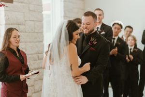 Bride and groom share a tender moment during wedding ceremony as officiant smiles beside them.