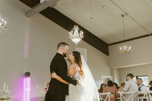 Bride and groom share their first dance under crystal chandeliers in a white wedding reception venue.