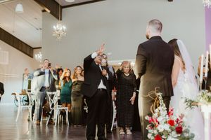 Wedding guests celebrate as father walks bride down the aisle in a chandelier-lit reception hall.