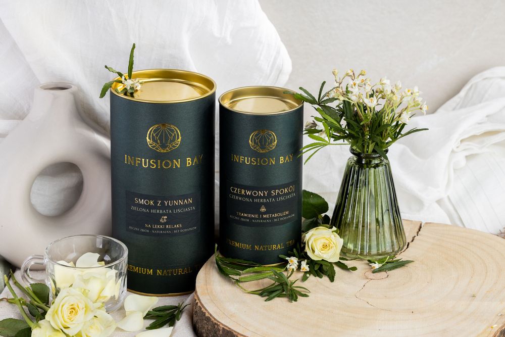 Two elegant Infusion Bar tea canisters displayed on a wooden slice with white roses and greenery.
