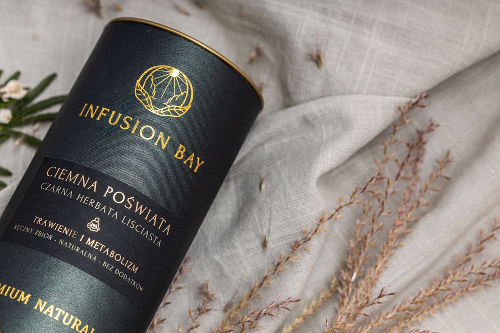 Infusion Bay Ciemna Poświata premium natural herbal tea in elegant black cylindrical packaging on linen fabric.