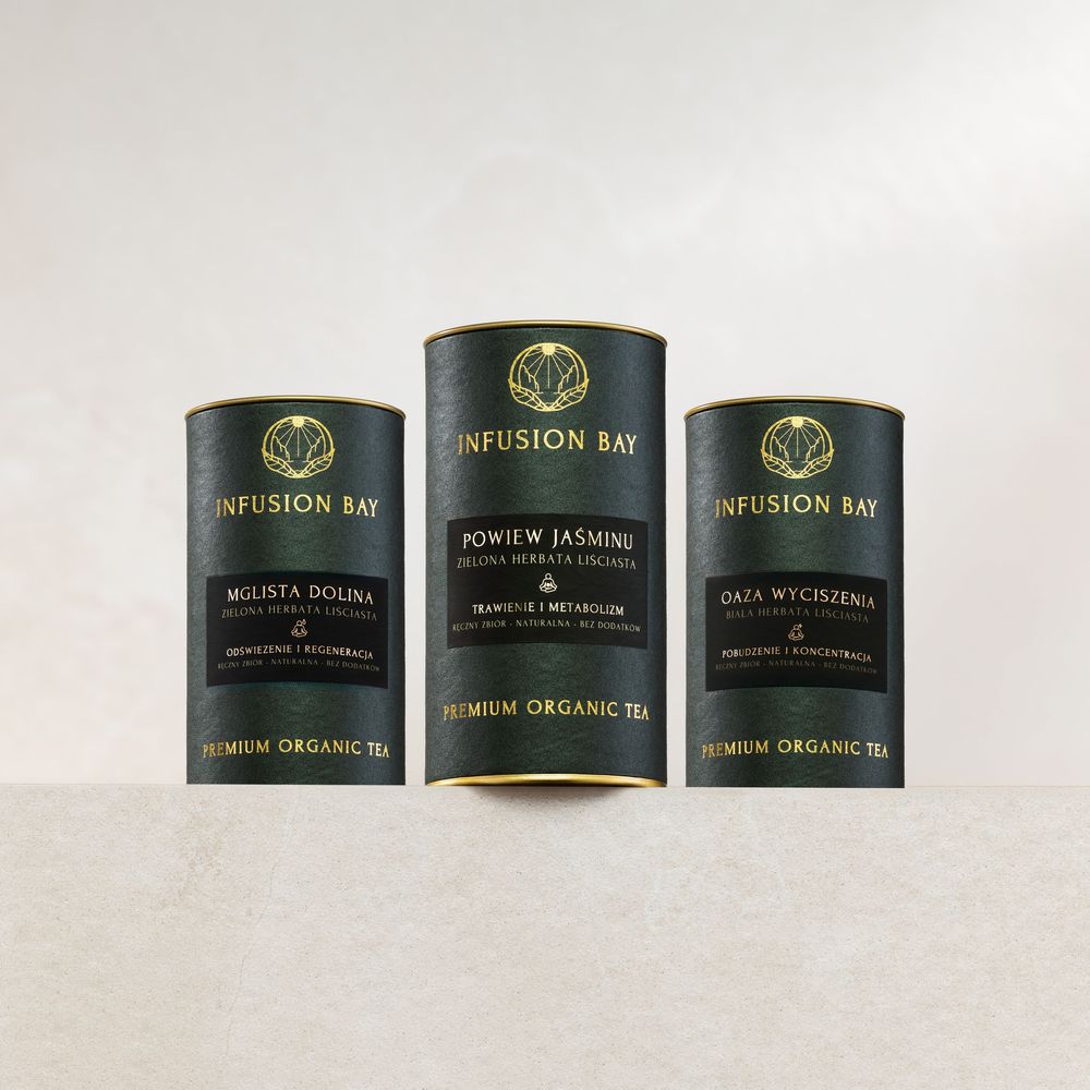 Three dark cylindrical Infusion Bay Premium Organic Tea canisters with gold lettering on a neutral background.