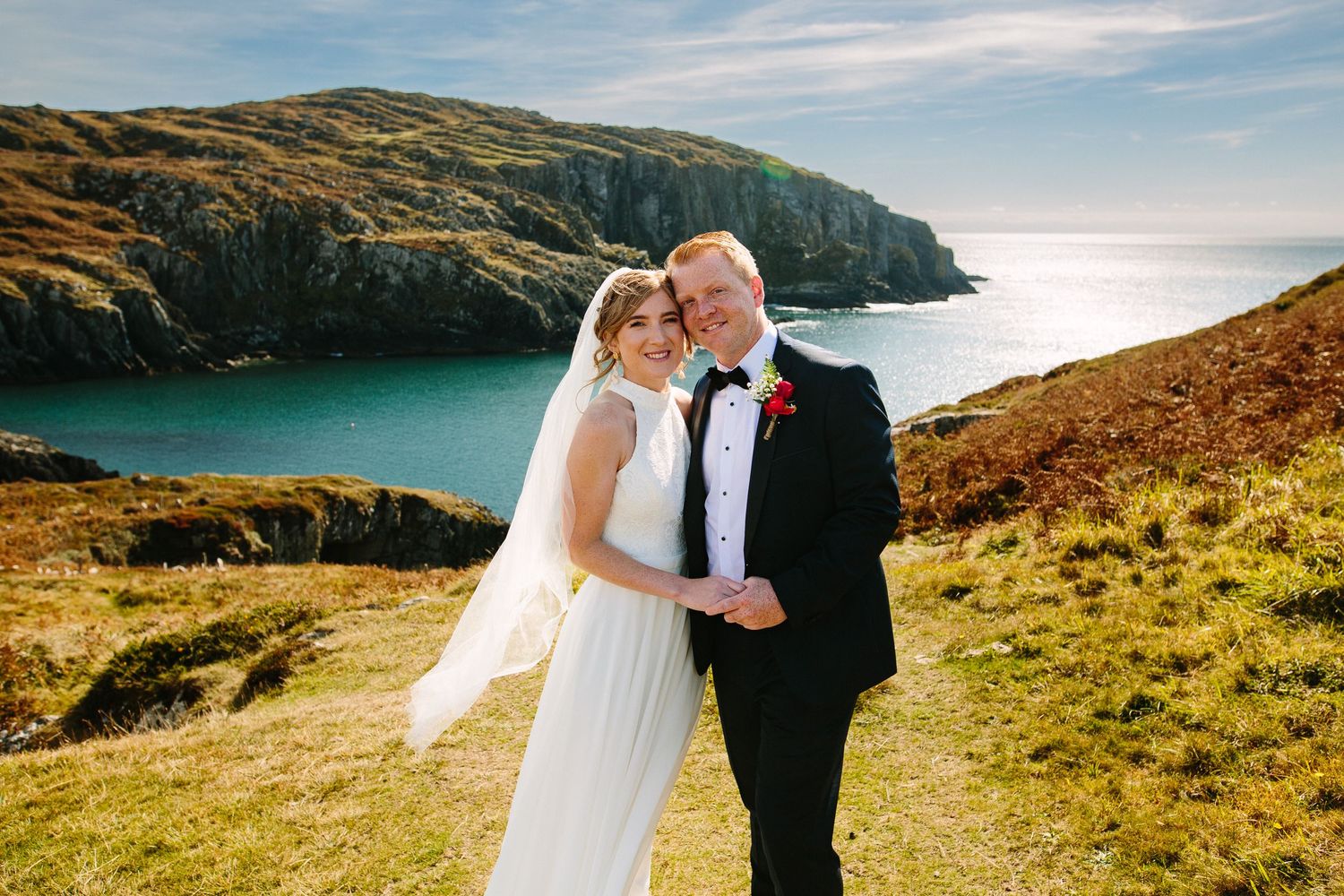 Bride and groom posing on Irish coastal cliffs with turquoise sea views on their wedding day.