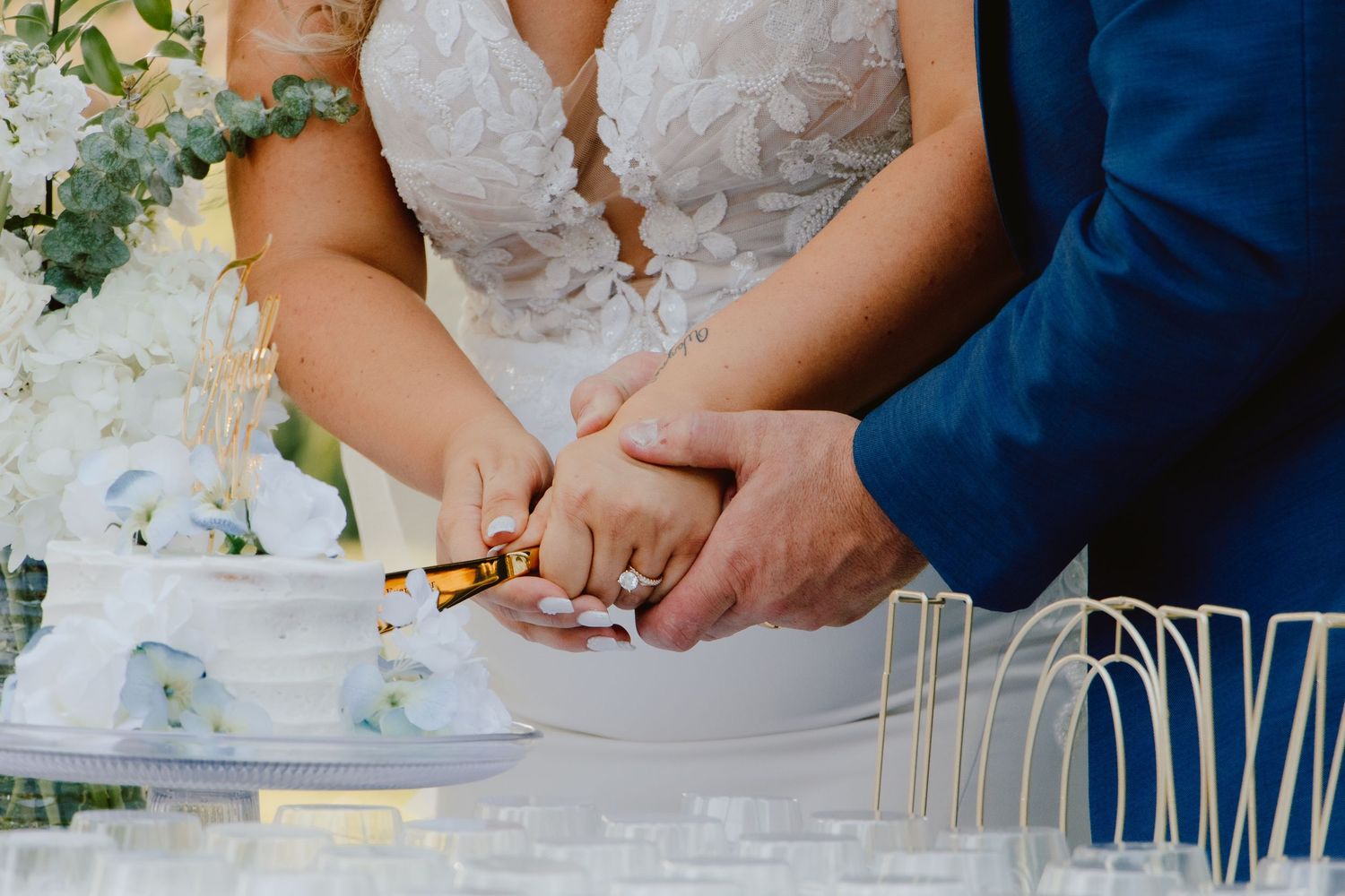 Bride and groom cutting their white wedding cake together, hands intertwined holding a knife at an elegant reception.