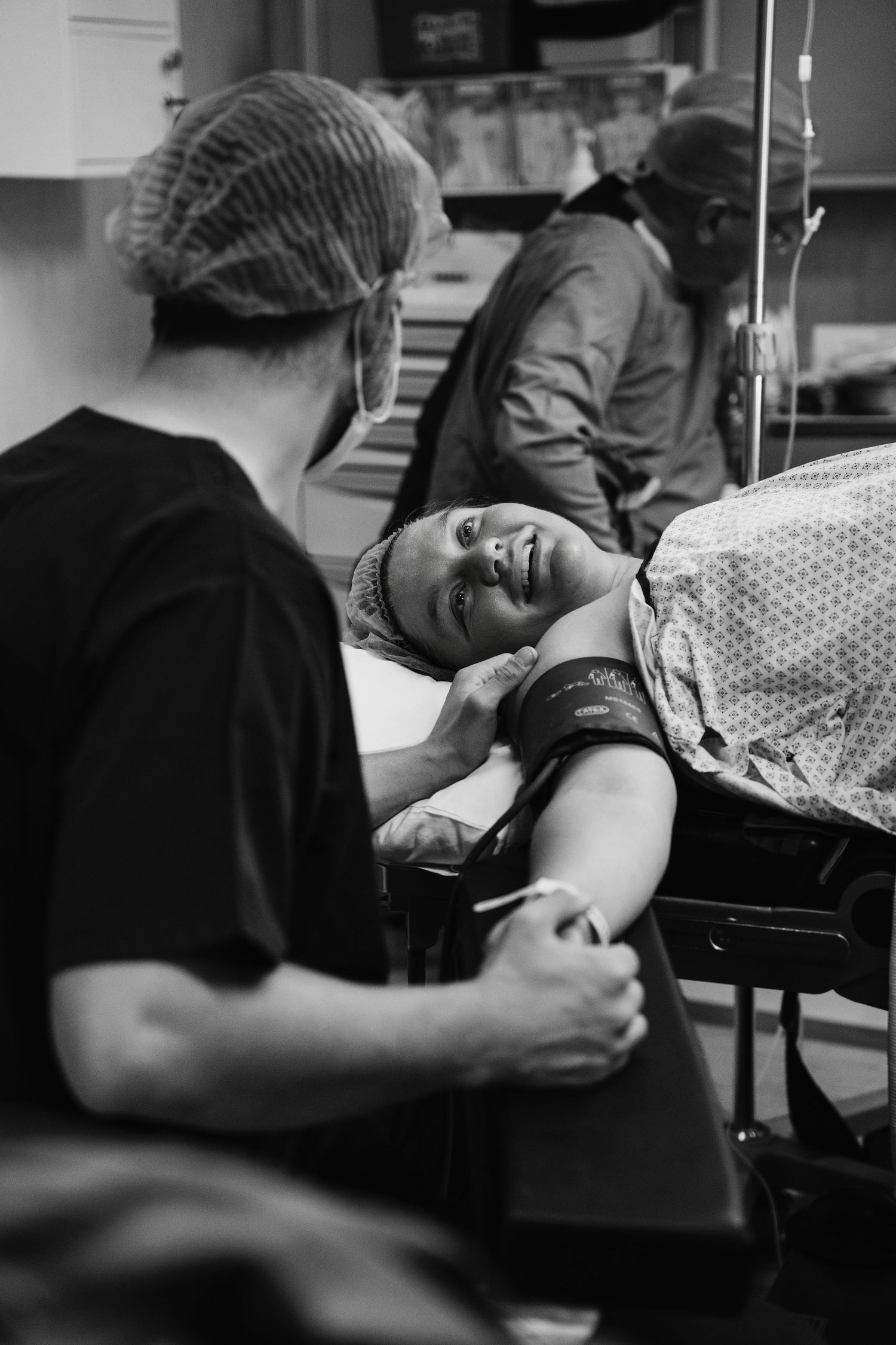 Black and white photo of a smiling patient on a hospital gurney with medical staff in scrubs and surgical caps nearby.