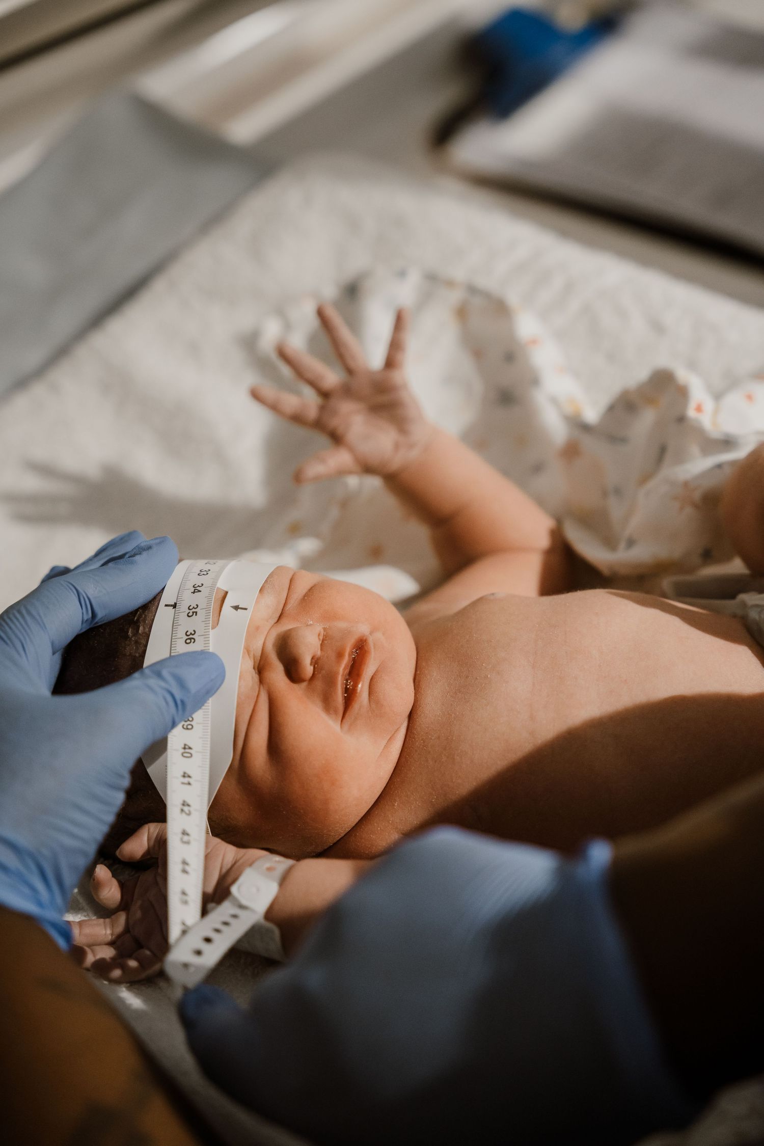 Medical professional measuring newborn baby's head circumference with tape measure after birth.