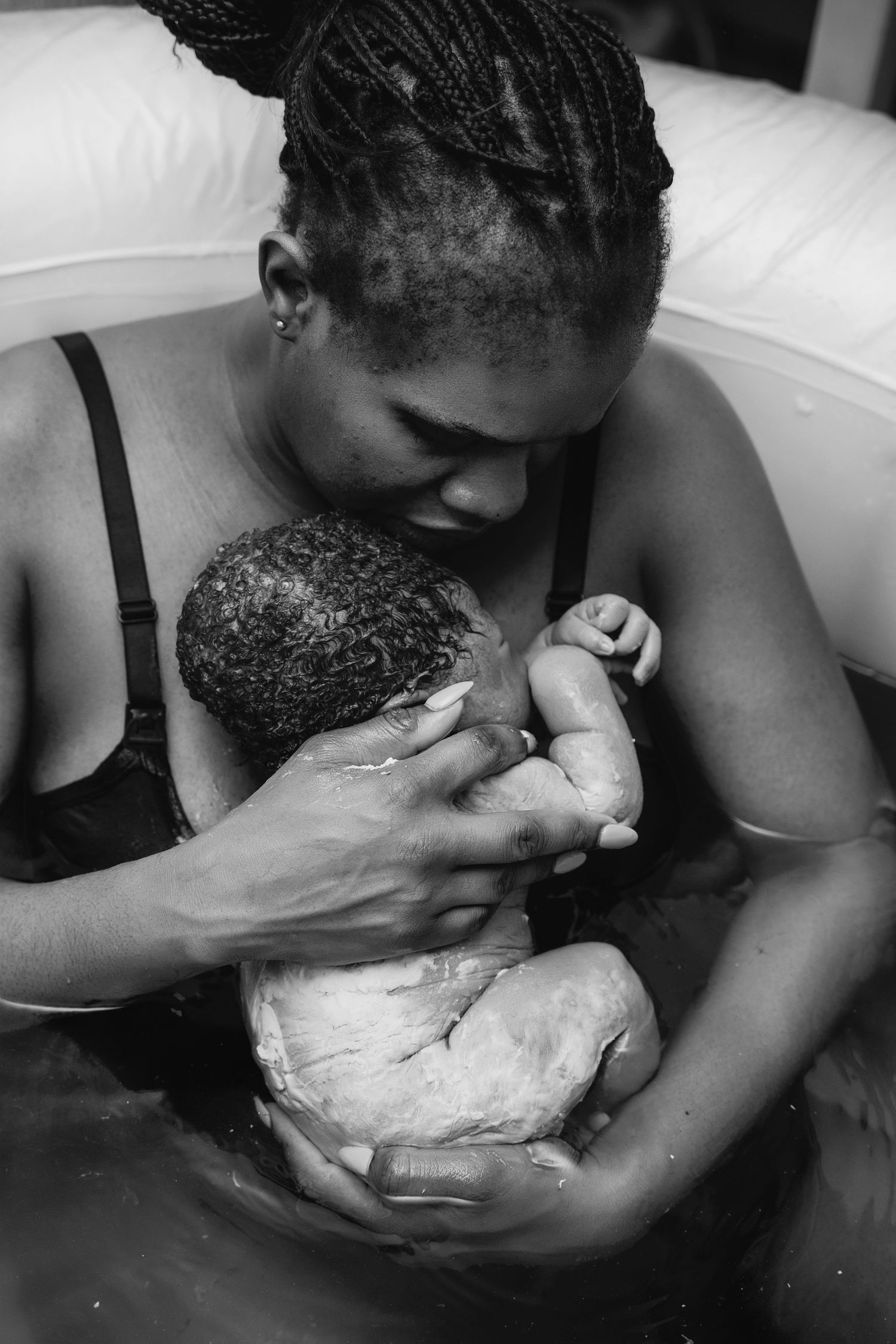 Black and white photo of a mother holding her newborn baby during a water birth, sharing a tender moment.
