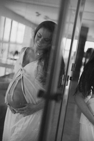 Black and white portrait of an expectant mother in a white dress smiling and cradling her baby bump.
