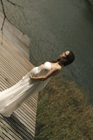 A person in a flowing white dress poses dramatically on wooden dock planks near dark water.